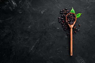 Raw beans in a wooden spoon on a black background. Top view. Free copy space. - Powered by Adobe