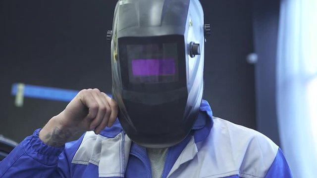 Portrait handsome specialist auto mechanic in welding helmet on the background of modern car service. Slow motion
