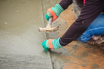 Grooving on concrete pavement by worker used deformed steel bar to stamp on concrete surface before the liquid concrete is solidified. Mason is grouting on concrete slabs to increase adhesion strength