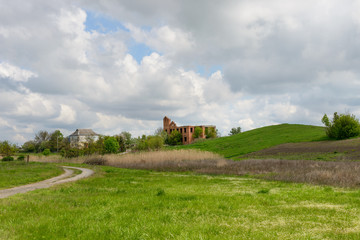 Rural landscape with unfinished brick building near grassy hill.