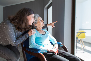 Adult daughter showing to senior mother scene out of window