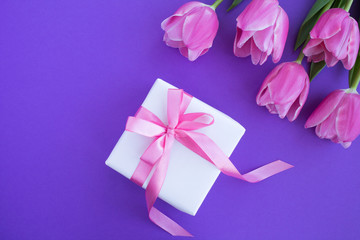 Gift with pink bow and pink tulips on the violet background.Top view.Copy space.