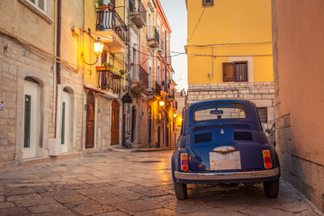 Scenic oldtown street and small retro blue car in Barletta city, Italy