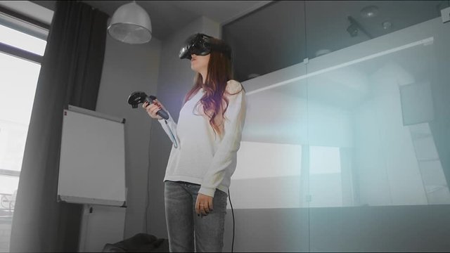 A young girl client studies the design project in virtual reality glasses, looks around, controls the joystick. The future of architecture and construction industry. Modern loft office. Red epic. 4K