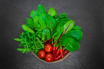 Composition of bunch wet vegetables places in bamboo bowl on black stone background