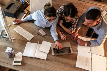 A group of casually dressed business professionals collaborate in the office, exchanging ideas and...