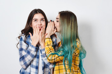 Two female friends gossiping. One girl tells the secrets of the other in her ear