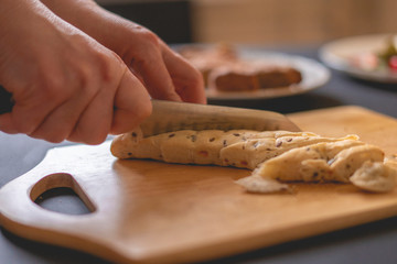 woman cuts bread with a knife in the kitchen on a wooden board