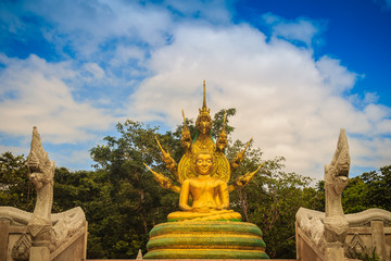 Fototapeta na wymiar Beautiful golden Buddha statue with seven Phaya Naga heads under white clouds and blue sky background. Outdoor golden seated Buddha image protected by 7 heads Naga spreads cover on top in cloudy days.