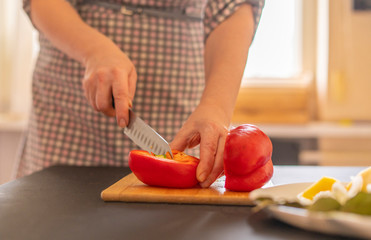 housekeeper cuts red pepper on a wooden board