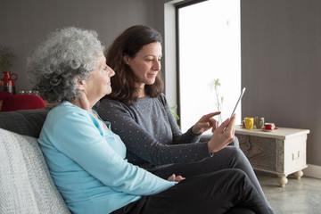 Serious elderly woman and her daughter browsing on tablet