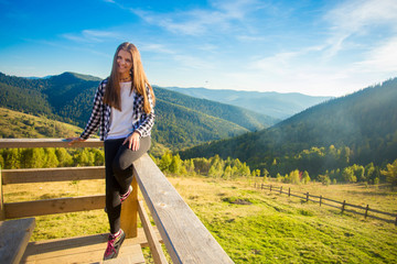 Fototapeta na wymiar Young woman with long hair on fence of terrace enjoy beautiful view of mountains