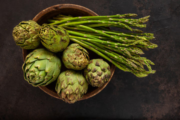 Close up photo of fresh artichoke in the old wooden bowl and Bunch of green asparagus. Top view on...