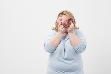 A fat, plump blonde woman on a white background, holding pink glazed donuts and a red apple.