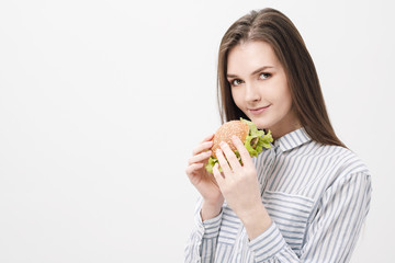 Young beautiful brunette girl on a white background with a hamburger in her hands.