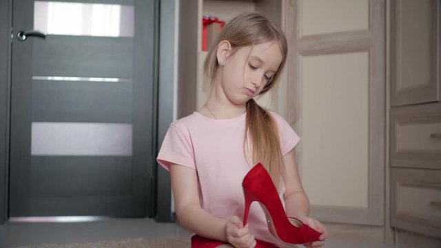 Little girl on the floor at home trying mom's red high heel shoes.
