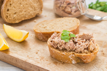Canned tuna served on fresh baguette with lemon and parsley decoration on wooden cutting board