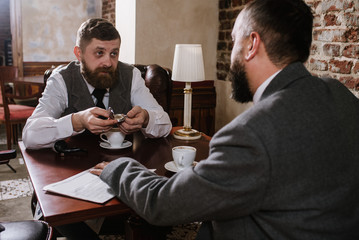 Two bearded men wearing old fashioned suits talking or discuss something in the restaurant