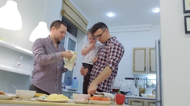Gay family with daughter kid cook pizza together in the kitchen.