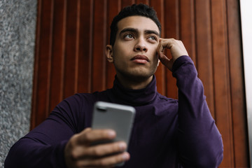 African American man with serious emotional face holding mobile phone and using mobile apps for job search, dreaming about successful career. Losing a job and unemployment stress concept. 