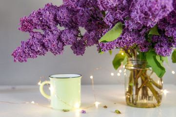 Lilac bouquet on the table with cups and festive lights