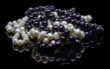 Two mixed strands of natural black pearl beads on a black background with reflection