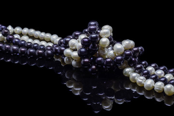 Two mixed strands of natural black pearl beads on a black background with reflection
