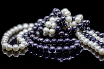 Two mixed strands of natural black pearl beads on a black background with reflection