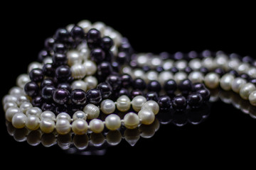 Two mixed strands of natural black pearl beads on a black background with reflection