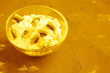 Homemade natural cottage cheese with kiwi in a glass bowl on a gray background.
