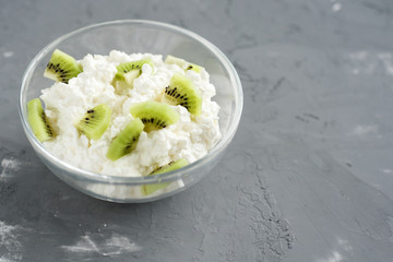 Homemade natural cottage cheese with kiwi in a glass bowl on a gray background.