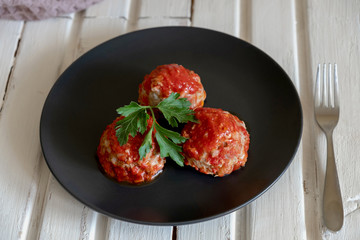 On a black plate are three meatballs in tomato sauce.