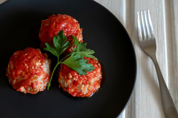 On a black plate are three meatballs in tomato sauce.