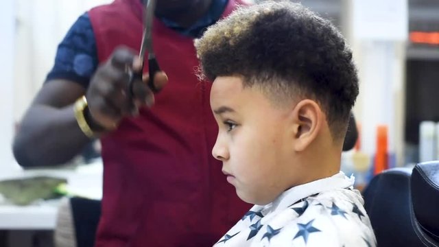 Boy in the african barbershop. Cute mixed boy makes a haircut in the African salon. Hair style. Haircut by machine for children. School boy hair style. Haircut 