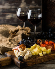 Assorted cheeses on wooden board plate. Camembert cheese, cheese grated bark of oak, hard cheese slices, walnuts, grapes, bread, thyme, top view. Cheese and wine. Antipasto. Red wine