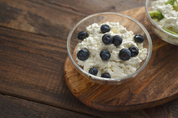 Close-up of bowl of cottage cheese and blueberries on natural wooden stand in the natural light