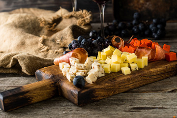 Assorted cheeses on wooden board plate. Camembert cheese, cheese grated bark of oak, hard cheese slices, walnuts, grapes, bread, thyme, top view. Cheese and wine. Antipasto. Red wine