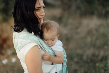 Mother wearing her sleeping child in carrier. Portrait of woman carrying her little baby in sling...