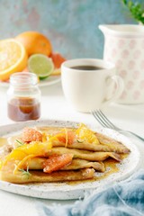 Pancakes crepe Suzette for breakfast with orange caramel sauce, orange slices, lime and orange zest and a cup of coffee. Dessert French cuisine. Sunday breakfast
