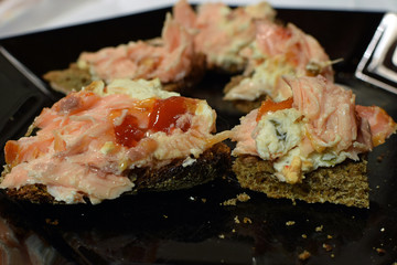 Rye bread with smoked salmon, chili sauce and blue cheese on black plate.