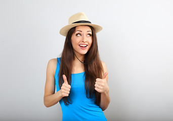Fototapeta premium Beautiful excited smiling casual woman in summer hat showing thumb up sign in bright blue top on blue copy space
