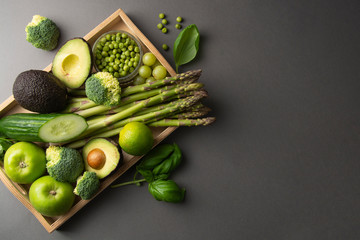 Green healthy food clean eating vegetables: asparagus, cucumber, basil, green peas, avocado, broccoli, lime, apples, grapes, broccoli on dark background, top view.