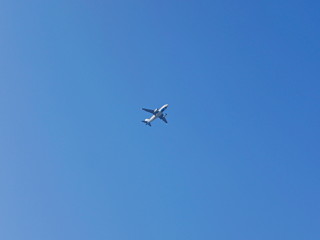 Fototapeta na wymiar An airplane flying across blue sky, from a far distance, in a sunny day in summer time