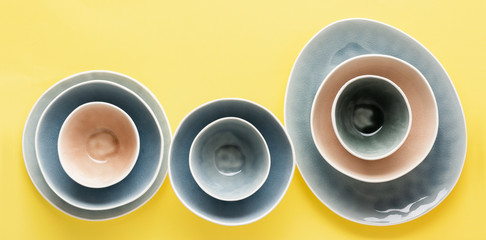 Beautiful blue, grey, beige dinnerware, plates bowls on yellow background table, top view, selective focus