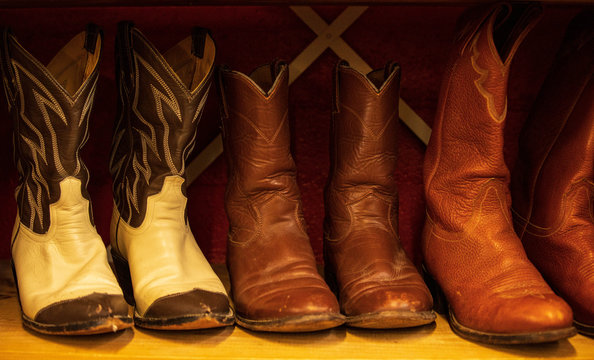 Three Pairs Of Rugged Leather Cowboy Boots On Shelf