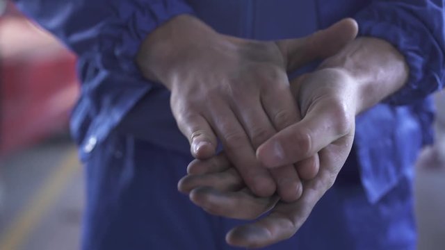 Unrecognized auto mechanic demonstrates his soiled hands after repairing a car in the service station. Close up.
