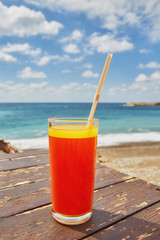 Melon juice on a sea beach. Glasses with red drink and straw stands on a fallen coconut.