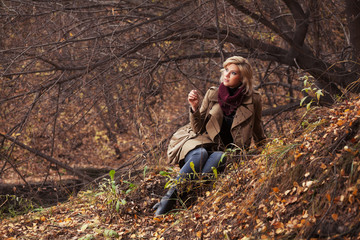 Naklejka na ściany i meble Happy young fashion woman with handbag sitting on ground in autumn park