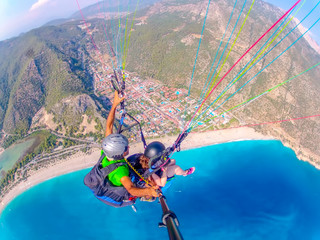 Paragliding in the sky. Paraglider tandem flying over the sea with blue water and mountains in...