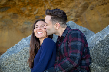 Fototapeta premium Happy Millennial Couple Sitting on Rocks Boyfriend Kissing Girlfriend
